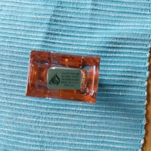 Lattafa Ana abiyedh coral  - Snygg parfymflaska från Lattafai genomskinligt glas med orange detaljer och svart fyrkantigt lock med guldring. Flaskan har en modern, rektangulär form och etikett med orientaliskt mönster. Perfekt för dig som gillar unika dofter och stilren design.Perfekt sommardoft.