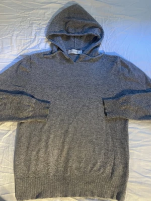 Grå cashmere hoodie från Sayless - Mjuk och lyxig grå hoodie från Sayless i 100% cashmere. Klassisk design med huva och ribbade muddar vid ärmslut och nederkant. Perfekt för dig som vill ha något riktigt bekvämt och stilrent i garderoben.  Skick: Mycket gott skick. • Färg: Gråmelerad. • Stil: "Old Money" / Minimalistisk / Casual chic. • Storlek: Xs.     Hör av dig vid frågor!
