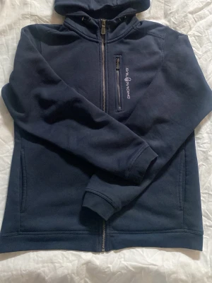 Mörkblå hoodie från Sail Racing - Mörkblå hoodie från Sail Racing. Säljer denna hoodie eftersom storleken inte passade mig och orkade inte lämna tillbaka så säljer den billigt, använt få gånger. Bra pris för en ny zip!