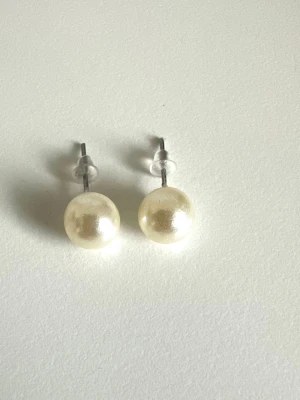 Klassiska pärlörhängen, helt nya - Stilrena pärlörhängen med rund form och vit skimrande färg. Syntetiska pärlor. Örhängena har metallstift och transparenta pluppar. Perfekta för dig som gillar enkel och elegant design. Helt nya i förpackning. 