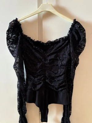 Svart body med puffärmar - Svart body med breda puffärmar och offshoulder-design. Från NLYone. Toppen är gjord i spetsmaterial med snygga rynkade detaljer framtill och en v-ringning. Passar perfekt för både vardagen och mer festliga tillfällen.
