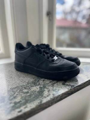 Nike Air Force 1 Low helsvart läder - Säljer ett par svarta Nike Air Force 1 Low i storlek 38. Skorna är i nyskick och bara använda ett få antal gånger och ser helt nya ut. En klassisk modell som passar till allt.  Orginalboxen finns tyvärr inte kvar. Perfekt för dig som vill ha ett par fräscha sneakers till ett bra pris. Hör av dig vid frågor!