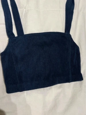 Mörkblå manchester linnetopp - Snygg mörkblå linnetopp i manchester med breda axelband. Toppen har en croppad passform och är perfekt att styla med höga jeans eller kjol. Enkel och stilren design som passar till många olika looks.