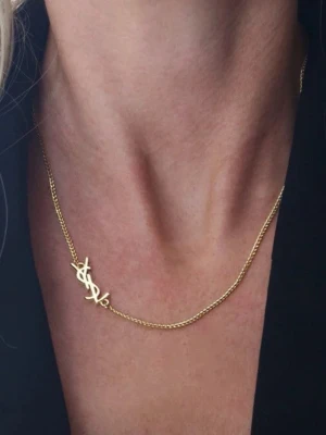 Guldhalsband med YSL-logga - Snyggt och stilrent halsband i guld med den ikoniska YSL-loggan som hänge. Kedjan är tunn och elegant, perfekt för att ge en lyxig touch till din outfit. Passar dig som gillar exklusiva accessoarer och vill sticka ut med ett klassiskt designerplagg.