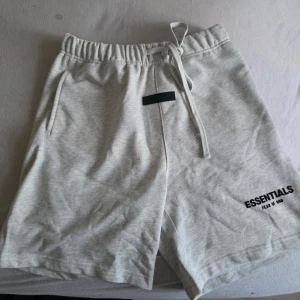  shorts från Essentials - Snygga ljusgrå shorts från Essentials Fear of God med resårmidja och snörning. Shortsen har fickor på sidorna och logga tryckt på vänster ben. Perfekta för en avslappnad stil.