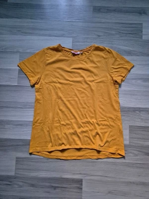 Gul basic t-shirt i bomull - En enkel gul t-shirt med rund hals och korta ärmar. Tillverkad i mjuk bomull som känns skön mot huden. Perfekt till jeans eller shorts för en avslappnad look. Ingen synlig logga eller tryck, bara clean och stilren design.