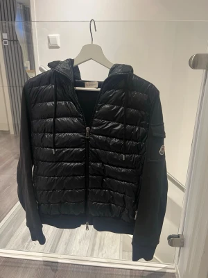 Svart cardiganjacka från Moncler - Snygg svart cardigan från Moncler med huva. Ärmarna är i mjukt tyg och har en ficka med Moncler-logga på vänster arm. Jackan har dragkedja framtill och ribbade muddar vid ärmslut och nederkant. Denna är använd endast ett fåtal gånger. Pris kan diskuteras💖