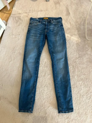 Blå slim fit jeans från Jack and Jones  - Säljer ett par klassiska blå slim fit jeans från Jack and jones. normal midja och snygga slitningar framtill för en trendig look. Tillverkade i mjuk denim med stretch för extra komfort. Waist 29 length 32