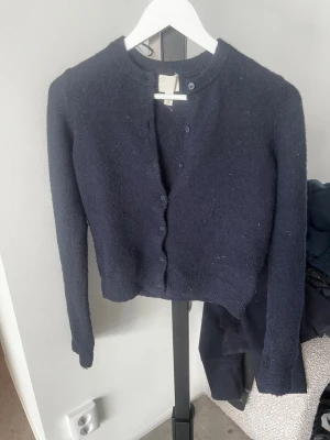Mörkblå kofta från H&M - Mörkblå, klassisk kofta från H&M med rund halsringning och knappar framtill. Koftan är stickad och har långa ärmar samt ribbade muddar vid hals och ärmslut. Perfekt att slänga över en t-shirt för en chill look.