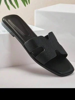 Svarta slip-in sandaler med H-design - Stilrena svarta sandaler med slip-in modell och bred rem i H-form. Sandalerna har en fyrkantig tå och är tillverkade i ett strukturerat syntetmaterial som ger en lyxig känsla. Perfekta för en trendig och avslappnad look. Beställde i storlek 37. Men storleken är 36or egentligen. De är för små och därmed säljer dom. De är helt nya oanvända 