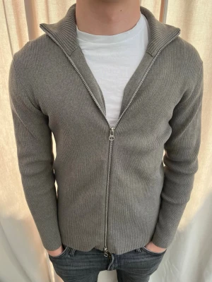 Grå ribbad ziptröja med hög krage - Sjukt snygg zip tröja från Ljung. Strl M, personen på bilden är 184 cm lång. Köptes för 1500 kr. Skicka gärna prisförslag. Kika in min profil för mer schyssta plagg.