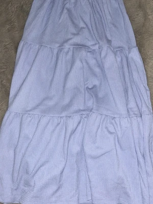 Ljusblå volangkjol med resårmidja - Supersöt ljusblå långkjol med volanger och bred resår i midjan. Kjolen har en luftig och flowy känsla, perfekt för varma dagar. Tillverkad i ett mjukt bomullsliknande material som känns bekvämt mot huden.