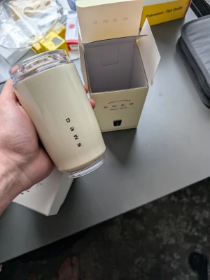 Smeg beige termosmugg - Säljer en stilren beige termosmugg från Smeg med svart logotyp på framsidan. Muggen har en cylindrisk form och transparent lock. Perfekt för att ta med dryck på språng. Levereras i originalförpackning.