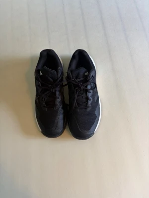 Svarta Adidas sneakers med mesh - Säljer ett par svarta Adidas sneakers med klassiska tre ränder på sidan. Skorna har en låg profil och är tillverkade i mesh och syntetmaterial med vit sula. Perfekta för dig som gillar sportig stil och komfort.