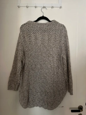 Grå stickad tröja - En grå stickad tröja med grovt hålmönster och långärmad design. Tröjan är oversized med rund hals och ribbstickade muddar vid ärmslut. Strl M-L.