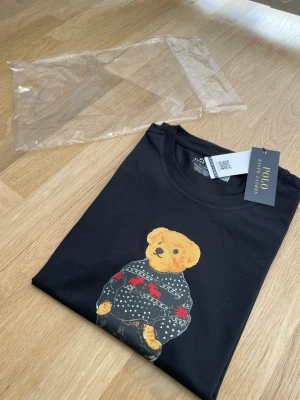 Ralph Lauren Polo Bear T-shirt Herr M Svart Ny med taggar - Ralph Lauren Polo Bear T-shirt – Dam/Herr – Svart – M/ 38/ 10 Ny med taggar. Äkta Ralph Lauren.  Aldrig använd, endast uppackad för bilder. Originalpåse medföljer. Passar både dam och herr i unisex passform.  Skick: Ny Storlek: M/ 38/ 10 Färg: Svart Modell: Polo Bear by Ralph Lauren  Priset är förhandlingsbart vid en snabb affär.