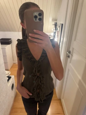 Brun ribbad volangtopp med knyt - Supersnygg brun ärmlös topp med ribbad struktur och volangdetaljer längs ärmhål och v-ringning. Knyt framtill för extra detalj. 