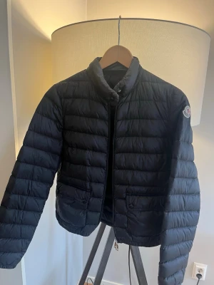  Moncler Lans jacka - Säljer en svart Moncler lans med klassisk quiltad design och hög krage. Jackan har två framfickor med knappstängning och Moncler-logga på vänster ärm. Perfekt inför våren. Inga skador eller fel men några bruks täcken. Ny pris 10 00 säljer för endast 2699! Hör av er vid minsta lilla fundering🤗