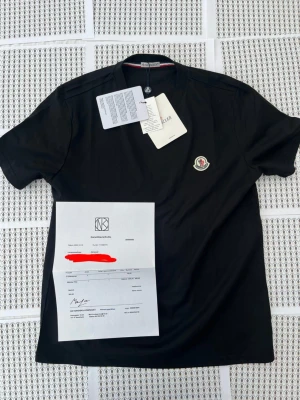 Svart Moncler t-shirt med logga - Snygg svart t-shirt från Moncler med klassisk rund hals och Moncler-logga broderad på bröstet. Tillverkad i mjuk bomull för en bekväm känsla. Perfekt till jeans eller shorts för en clean och stilren look.