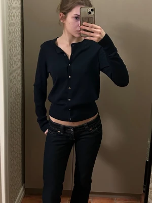 Mörkblå klassisk kofta med knappar - Snygg mörkblå kofta med rund hals och silverfärgade knappar framtill. Modellen är figurnära och har långa ärmar. Perfekt att bära både stängd och öppen över ett linne eller t-shirt. Materialet är mjukt och stretchigt.