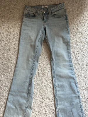 Lowwaist bootcut jeans från Gina Tricot - Säljer ett par ljusblå lowwaist bootcut jeans från Gina Tricot. Jeansen har klassisk femficksmodell, snygga detaljer med ficklock bak och silverfärgade knappar. Tillverkade i mjuk denim med skön stretch. Perfekta för en avslappnad och trendig look.