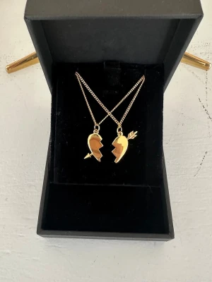 Arrow heart necklace  -  Två matchande guld halsband med delade hjärthängen – perfekta att dela med en vän eller partner. Halsbanden är 100 % rost- och nickelfria. Kedjorna är 40 cm långa men kan förlängas med ytterligare 5 cm. Hör gärna av dig om du har några frågor ☺️
