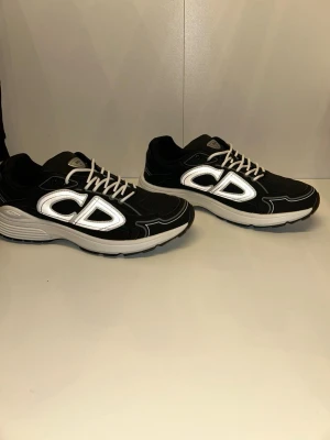 Svart vita b30 sneakers  - Snygga svarta sneakers från b30 med stora vita CD-loggor på sidorna och vita snören. Skorna har en chunky vit sula och ovandel i mesh och syntetmaterial. Perfekta för dig som vill sticka ut med en exklusiv och trendig look.