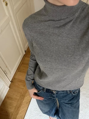 Grå polotröja - Snygg grå  polotröja med lång ärm och ribbad hög krage. Tröjan har en klassisk rak passform och är tillverkad i mjukt material som känns skönt mot huden. Perfekt att styla med jeans eller kjol för en clean look.