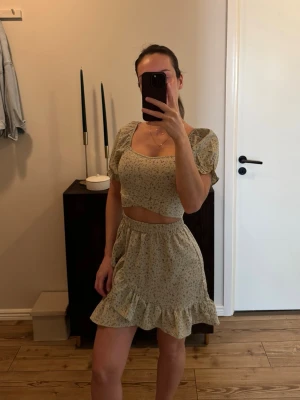 Blommigt set. Kjol och topp. - Sött tvådelat set i ljusgrönt med småblommigt mönster. Toppen har puffärmar och fyrkantig ringning, kjolen är kort med volangkant och resår i midjan. Perfekt för sommarens alla tillfällen. 