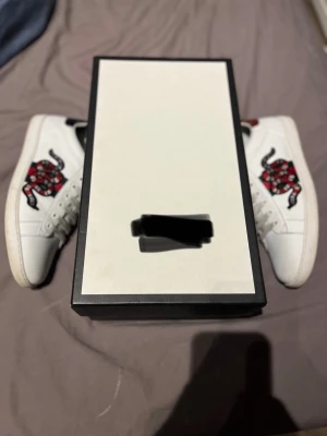 Ace skor med orm  - Säljer ett par vita  sneakers i läder med den ikoniska gröna och röda sidoremsan samt en broderad röd orm på sidan. Klassisk låg modell med vita snören och gummisula. Perfekta för dig som vill sticka ut med lyxig streetstyle. Ej sko box ingår 