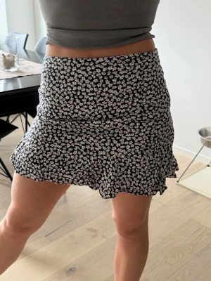 Blommig kortkjol från Abercrombie & Fitch - Supersöt kortkjol från Abercrombie & Fitch med mörkblå botten och små vita blommor. Kjolen har volangkant nedtill och sitter tajt upptill för en snygg siluett. Perfekt för sommaren!✨☀️🥰