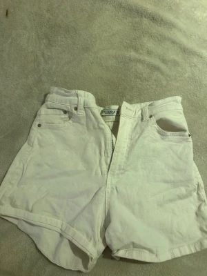 Vita högmidjade shorts från Pull&Bear - Säljer ett par vita högmidjade shorts från Pull&Bear. De har klassisk femficksdesign, dragkedja och knapp framtill. Materialet är mjuk bomull och passformen är normal. Perfekta för varma sommardagar! Pris kan diskuteras