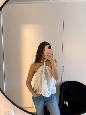 Vit halterneck topp med öppen rygg - Säljer en luftig vit halterneck topp och knyt i nacken. Toppen är ärmlös och har öppen rygg, perfekt för varma dagar. Passformen är loose och materialet känns som bomull. Superfin till jeans eller kjol!