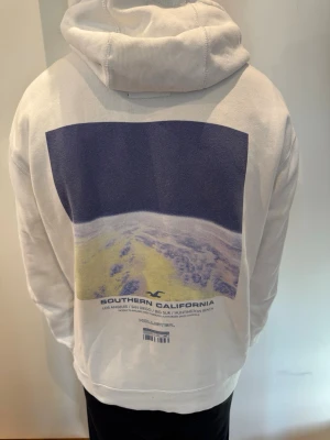 Vit Hollister Hoodie - Säljer en riktigt fräsch vit Hollister Hoodie i storlek M. Modellen är 180 cm och väger 65 kg.