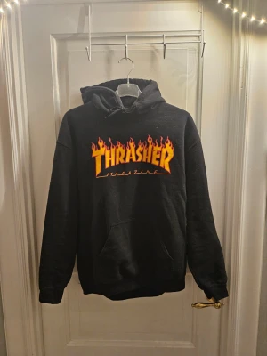 Svart Thrasher hoodie med flames - Svart hoodie från Thrasher med ikoniskt flames-tryck i gult och rött på bröstet. Klassisk känguruficka framtill och justerbar huva. Den är i nyskick och köptes för 600 kr. Kan köpas tillsammans med peak tröja för 1400 kr 