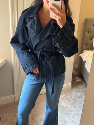 Mörkblå jeansjacka med skärp från mango - Snygg mörkblå jeansjacka med skärp i midjan och coola detaljer vid ärmsluten. 