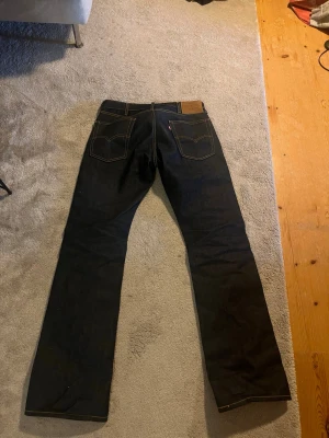Levis Bootcut jeans 517 blåa - Säljer ett par klassiska mörkblå jeans från Levi's med raka ben och kontrastsömmar. Jeansen har fem fickor, läderpatch bak i midjan och den ikoniska röda Levi's-lappen på bakfickan. Tillverkade i slitstark denim, perfekta för en clean och tidlös look. Storleken är 29W/32L