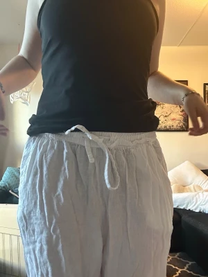 Vita linnebyxor - Säljer ett par luftiga vita linnebyxor med avslappnad passform och dragsko i midjan. Perfekta för varma dagar och ger en chill vibe till din outfit. Materialet är tunt och svalt linne som känns skönt mot huden.