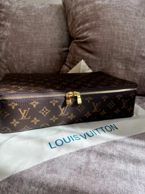Louis Vuitton Monogram sminkväska  - Snygg sminkväska från Louis Vuitton i klassiskt brunt monogrammönster med guldiga dragkedjor. Väskan har en rektangulär form och är tillverkad i tåligt canvasmaterial med exklusiva detaljer. Perfekt för dig som gillar lyxiga accessoarer.