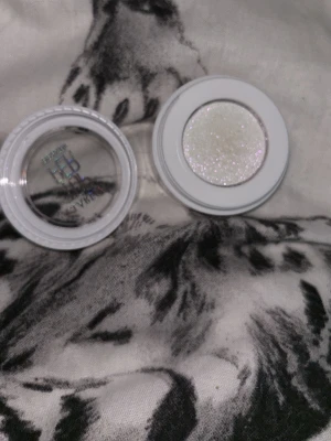 VIT GLITTRIG ÖGONSKUGGA LARESA - Supersnygg vit ögonskugga från LARESA med intensivt glitter och holografisk effekt. Kommer i en rund plastburk med genomskinligt lock där det står 'TOPPER'. Perfekt för att skapa en skimrande look och highlighta ögonen.