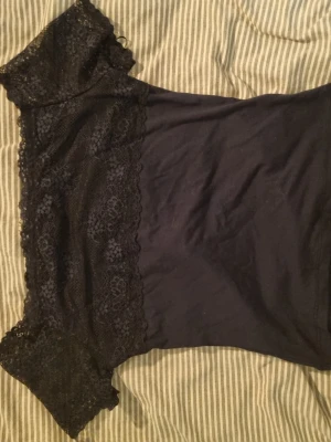 Marin blå spets topp med offshoulder - Snygg svart topp med offshoulder-design och detaljer i spets. Toppen har korta ärmar och en figurnära passform. Perfekt att styla med jeans eller kjol för en trendig look.