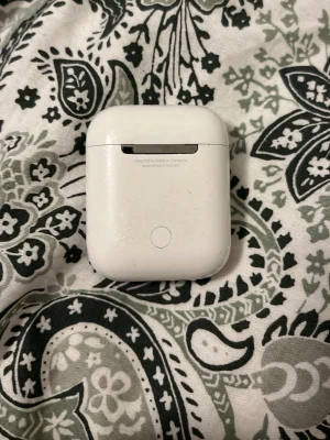 Apple AirPods gen 2 - Säljer ett par vita Apple AirPods med tillhörande laddningsetui. De är trådlösa in-ear hörlurar i klassisk Apple-design med slimmad form och smidig magnetisk laddningsbox i plast. Perfekta för musik, samtal och träning. Gammal version 