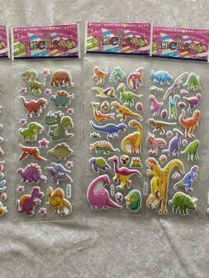 Färgglada dinosaurieklistermärken - Säljer flera ark med klistermärken i form av olika dinosaurier i färger som lila, grön, gul, orange och blå. Motiven är tecknade och har söta uttryck, vissa med stjärnor och ägg. Perfekt för att dekorera anteckningsböcker, datorer eller mobilskal.