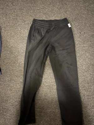 Svarta mjukisbyxor med dragsko - Säljer ett par svarta mjukisbyxor med resår i midjan och dragsko för skön passform. Byxorna har raka ben och är tillverkade i ett mjukt och bekvämt material, perfekta för chill dagar. Enkla att matcha med hoodie eller t-shirt.