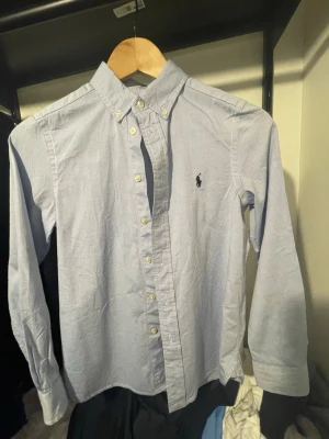 Ljusblå Ralph Lauren skjorta - Säljer en ljusblå ralph Lauren Skjorta i storlek 12. Passar ca 150-168. Använd Max 2 gånger. Kom gärna med frågor och funderingar.
