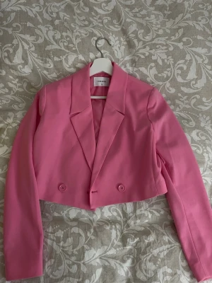 Kort rosa kavaj från Terranova  - Trendig kort kavaj i starkt rosa från Stradivarius. Kavajen har dubbelknäppning framtill, klassisk krage och långa ärmar. 