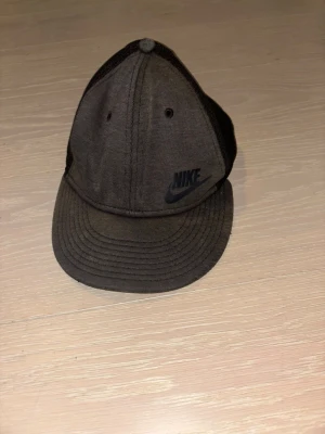 Svart Nike keps med mesh - Snygg svart keps från Nike med klassisk böjd skärm och mesh-paneler på sidorna för extra ventilation. Framtill finns en diskret Nike-logga i svart. Kepsen har justerbar snapback baktill och är tillverkad i bomull och mesh.