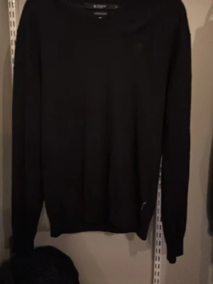 Svart stickad tröja med V-ringning - En klassisk svart stickad tröja med V-ringad hals och långa ärmar. Tröjan har en enkel och stilren design, perfekt att matcha med jeans eller kjol. Ribbstickade muddar vid ärmslut och nederkant ger en snygg passform. Storlek XL/L