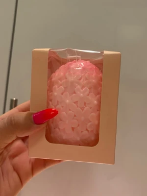 Rosa blomformad dekorljus - Säljer ett dekorativt ljus i form av ett ägg, täckt med små blommor. Ljusets färg är ljusrosa och det kommer i en söt presentförpackning med genomskinligt fönster. Perfekt som inredningsdetalj eller present.