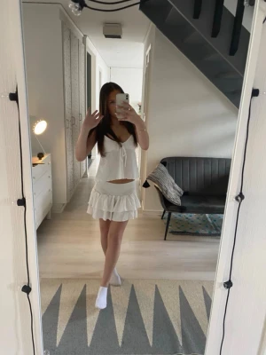 Vit linnetopp med knyt och v-ringning - Söt vit linnetopp med v-ringning och knyt framtill. Toppen är ärmlös och har en luftig, flowy passform som passar perfekt till sommaren. Tillverkad i ett lätt material som känns skönt mot huden. Enkel att matcha med kjol eller jeans.